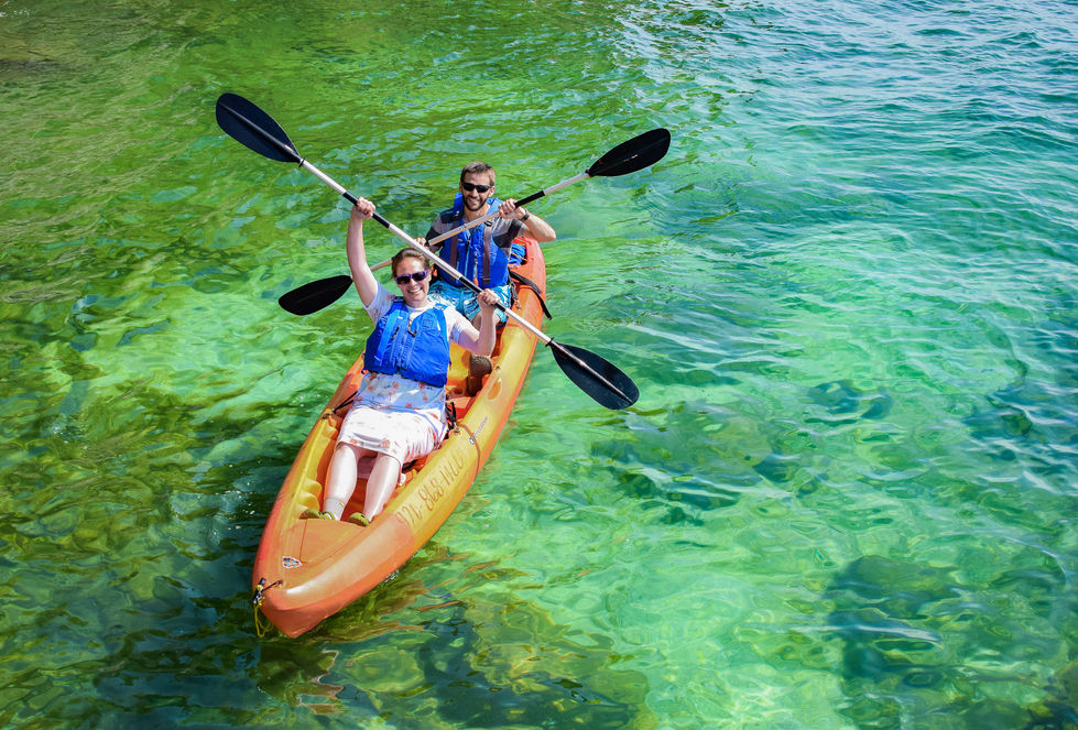 tandem kayakers on green, clear water holding paddles criss crossing and smiling — tour photography by Shutter & Sojourn