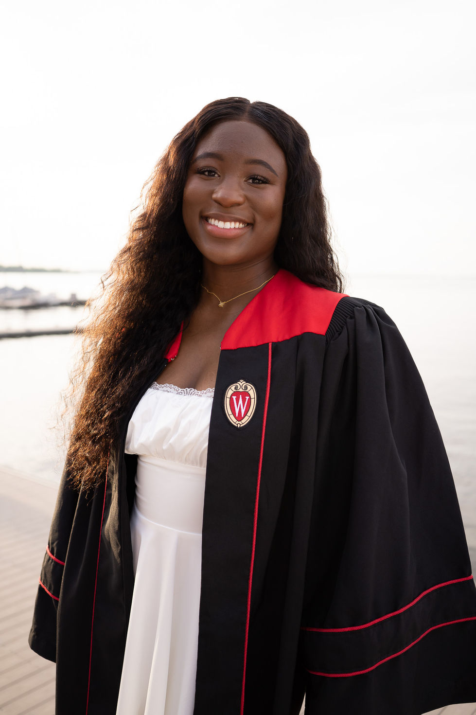 college graduate smiling in gown and white dress by waterfront High school senior boy looking off into the distance in green field — graduation photography by Shutter & Sojourn
