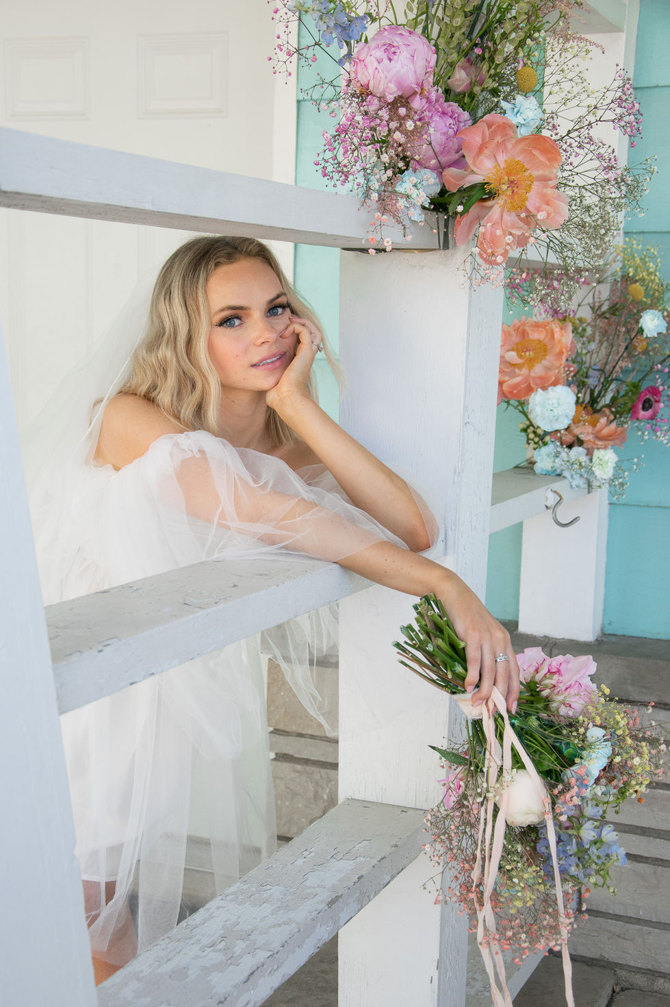 bride leaning over wall with her head on one hand and the other drapes her flowers over the wall — wedding photography by Shutter & Sojourn