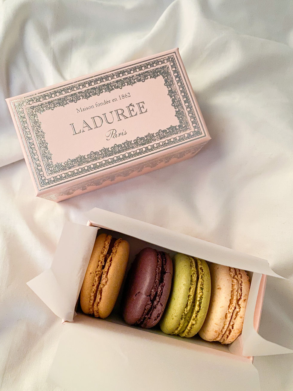 various colored macarons in a dainty, pink laduree box sitting on white sheets — travel photography by Shutter & Sojourn