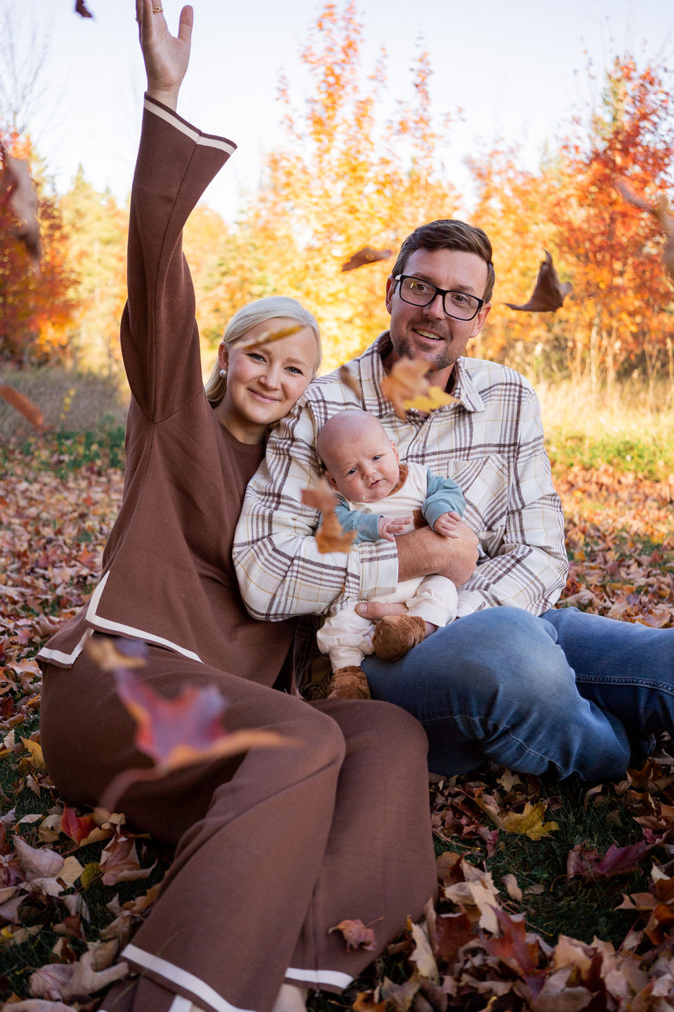 woman throwing leaves in the air while husband holds baby and smiles with orange and yellow fall trees — family photography by Shutter & Sojourn