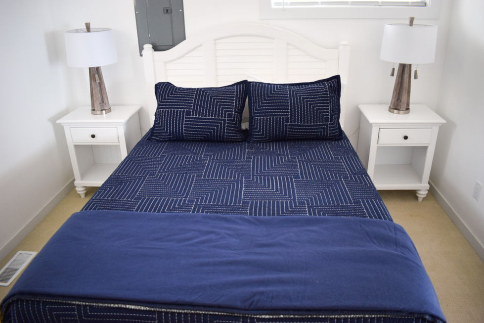 navy quilted queen bed bookmarked with 2 white nightstands and silver lamps — real estate photography by Shutter & Sojourn