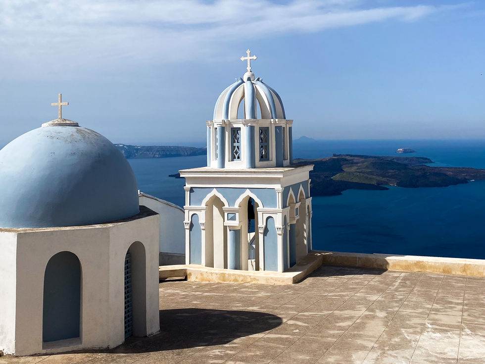 light blue and white church steeple at edge of cliff looking out at sea and islands