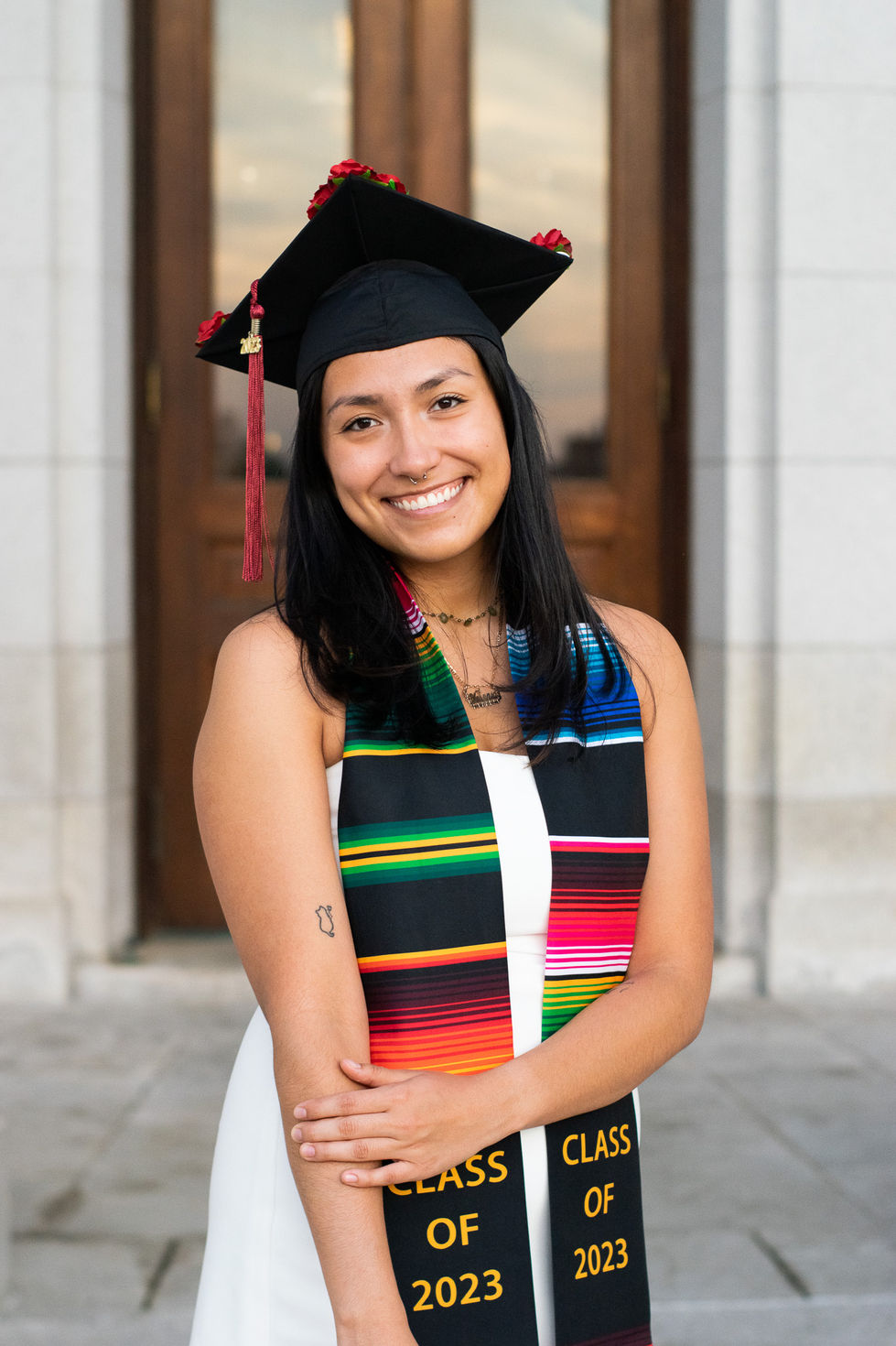 College graduate holding arm and smiling with cap on and colorful ribbon High school senior boy looking off into the distance in green field — graduation photography by Shutter & Sojourn