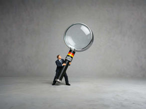 Mann in schwarzer Geschäftskleidung hält eine riesige Lupe mit seinen Händen fest. Auf der Lupe ist die Deutschlandflagge und das Jahr 2026 angehaftet. Repräsentiert Online-Sichtbarkeit im Jahr 2026. Semiotik Studio