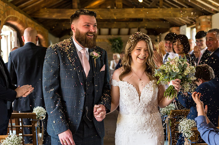 Bride and groom walk down the aisle with guests throwing confetti