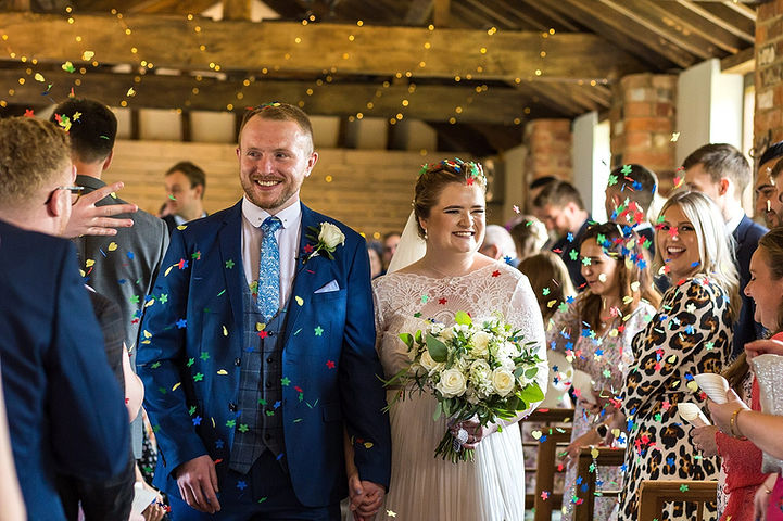 Bride and groom walk down the aisle with guests throwing confetti