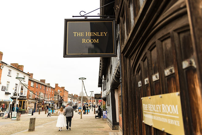 Bride and groom in the background with The Henley Room building and sign in the foreground