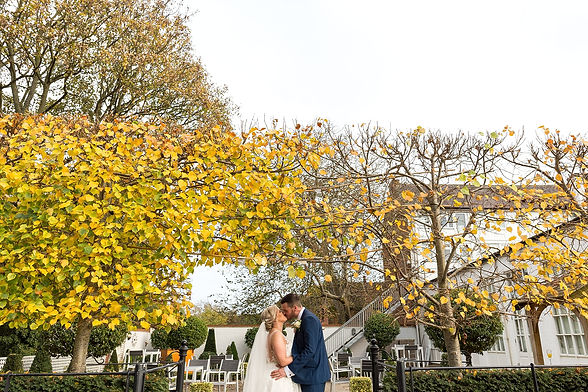 Bride and groom kiss in the garden at Warwick House with autumn leaves on the trees