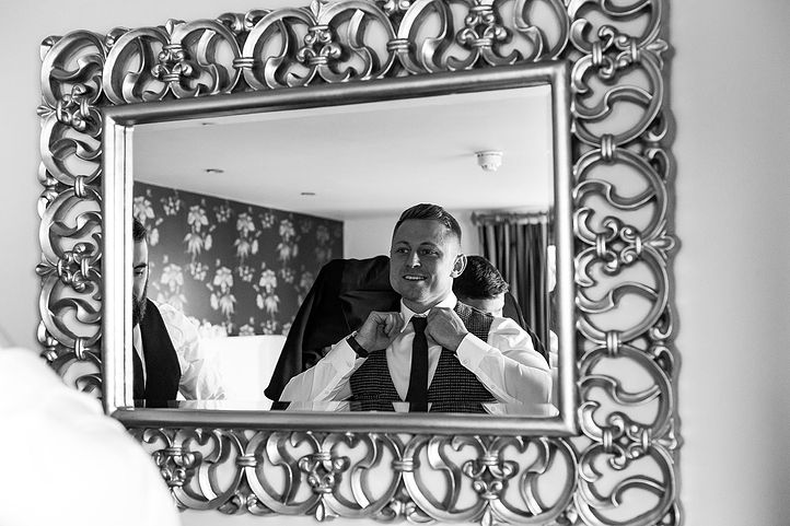 Groom adjusts his tie in the mirror