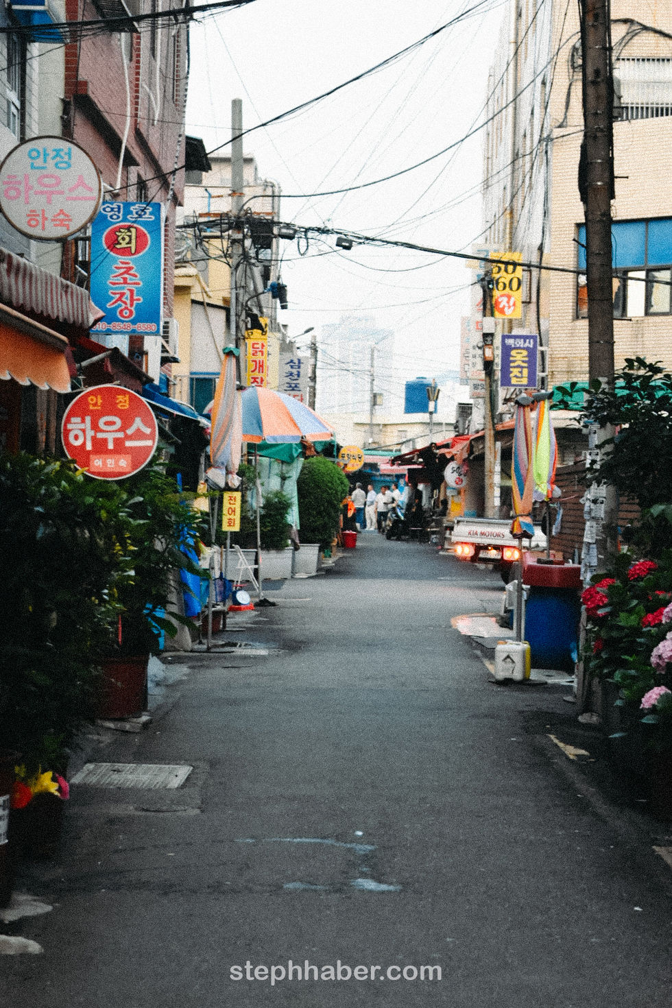 Narrow street with colorful signs and umbrellas.