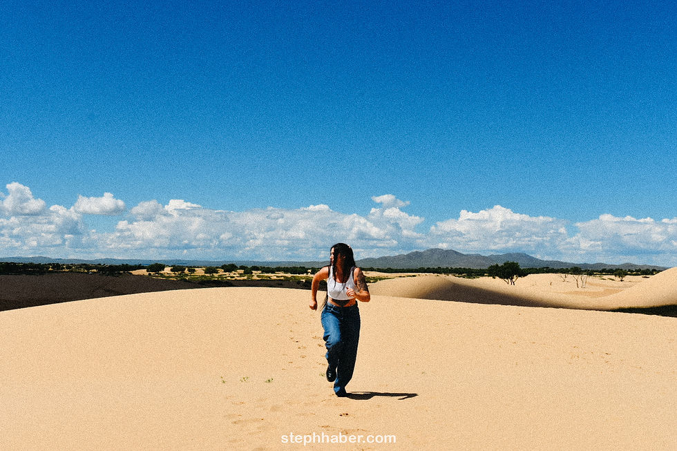 Woman in a white top and jeans runs on sandy dunes under a clear blue sky with distant mountains. Text: stephhaber.com.