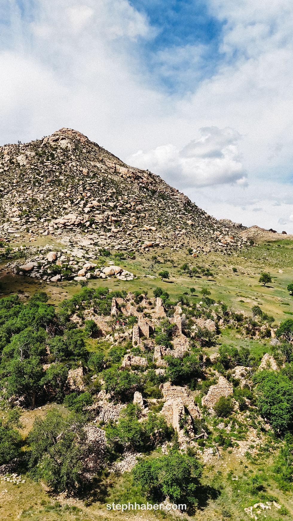 Ruins of stone structures surrounded by green vegetation, set against a rocky hillside under a blue sky. Text: stephhaber.com.