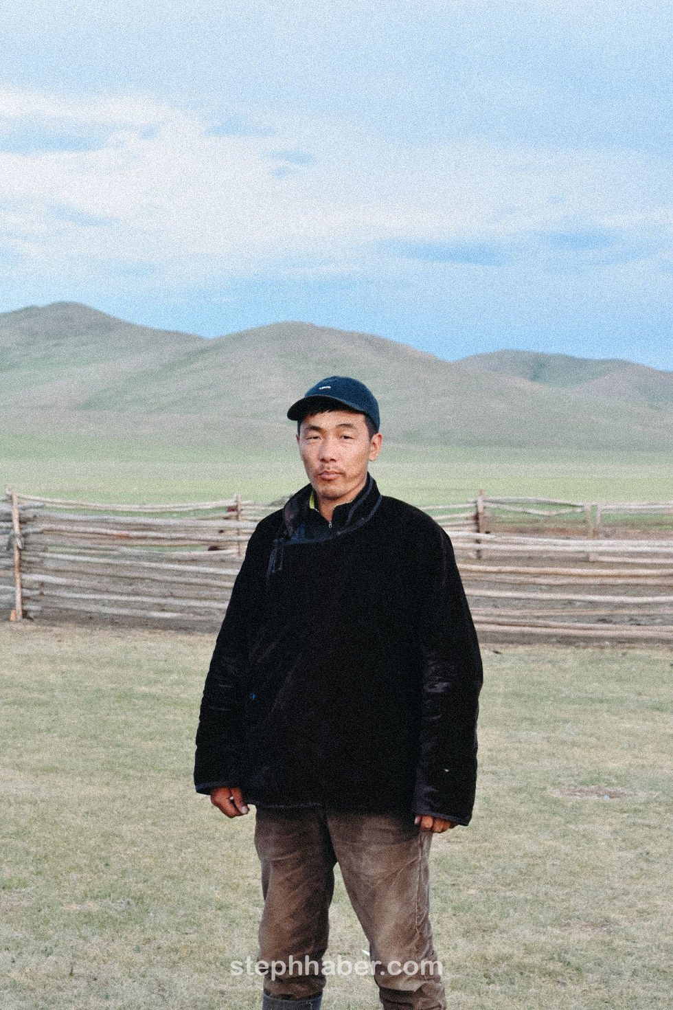 Man standing in front of wooden fence, rural landscape.