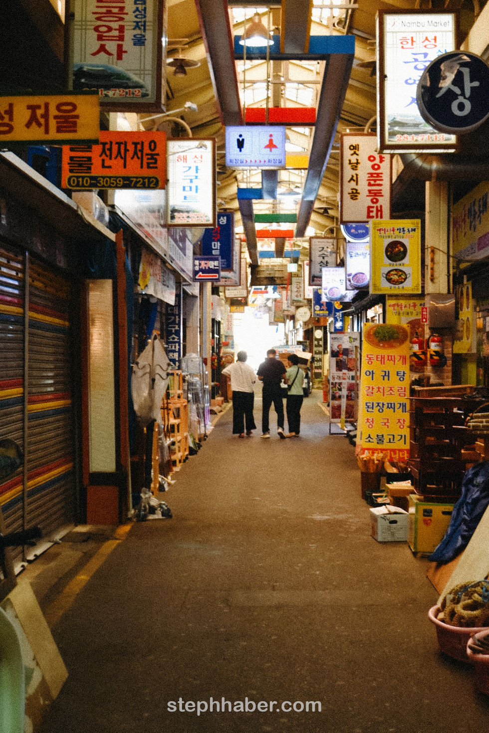 Bustling market alley with colorful signs and people.