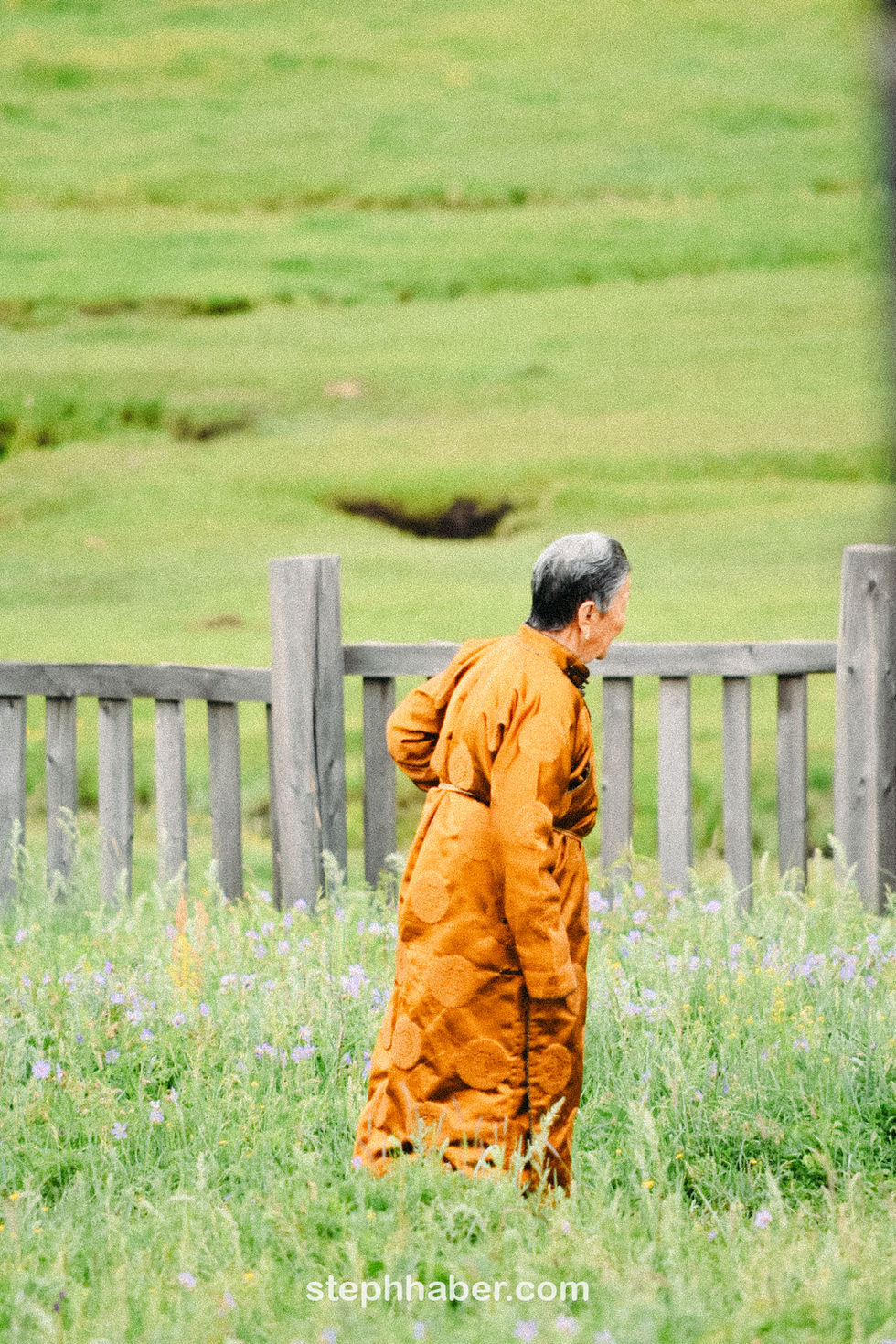 Person in orange robe walking by wooden fence.