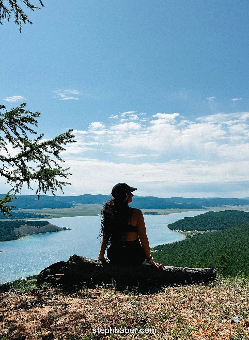 Woman in a cap sits on a log, overlooking a scenic lake and mountains under a clear blue sky. Calm atmosphere. lake kovsgol mongolia