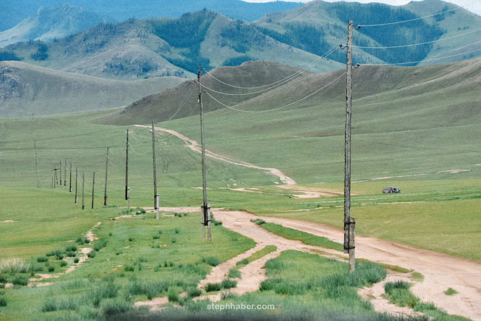 Dirt road with utility poles in hilly landscape. Mongolia