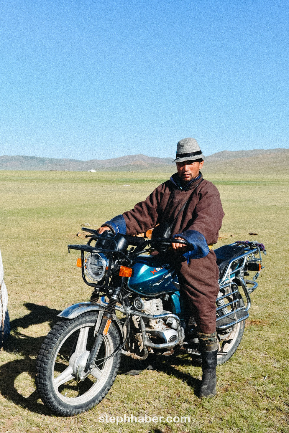 Person on motorcycle in open landscape, wearing a hat.