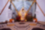 A beautiful altar inside of a dome, with dishes of herbs on it, and vases of flowers on either side. There is a magical symbol in the middle. There are baskets on either side of the altar, with one side asking "what are you letting go of?" and the other asking "what are you transforming into?"