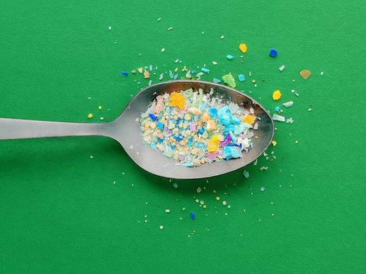 Spoon on green background with colorful microplastic particles scattered around, indicating pollution within food.