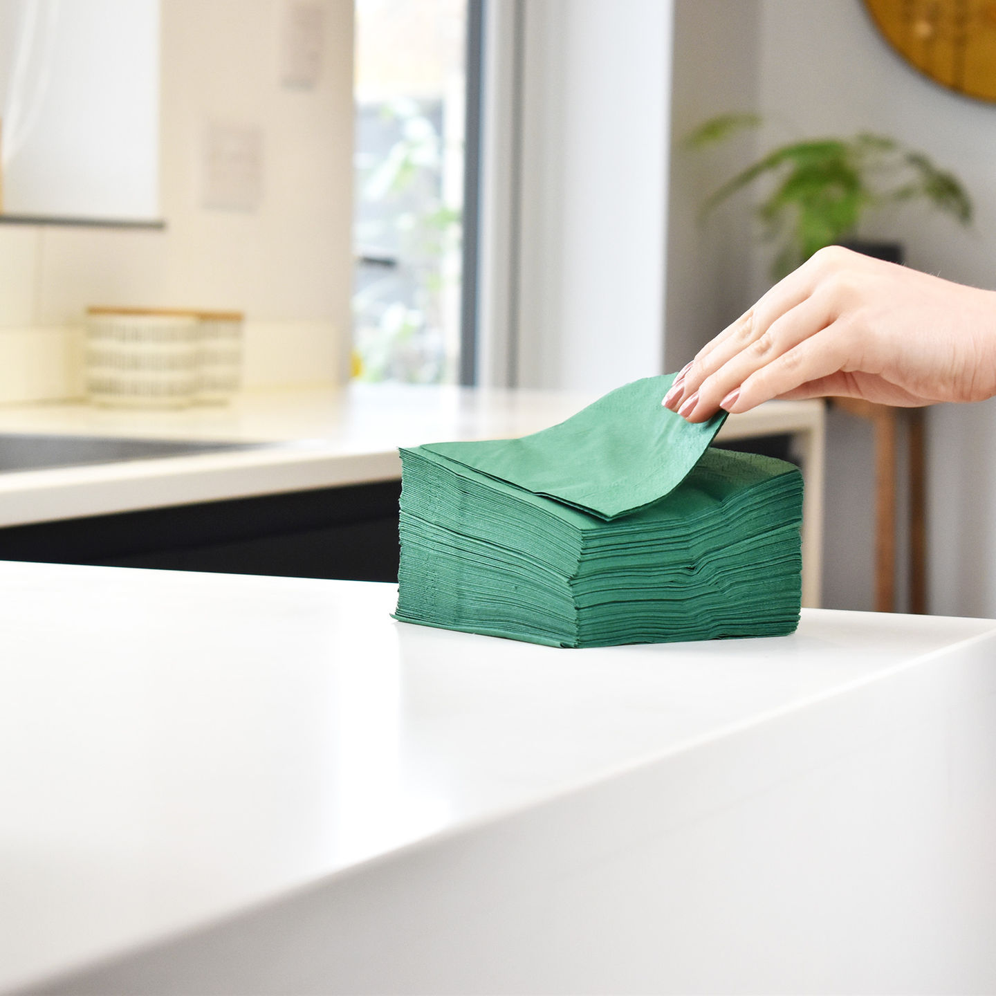A hand picking up a green paper napkin from a stack of napkins