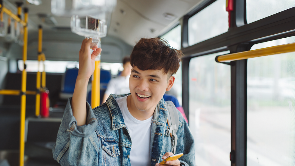 Smiling Loughborough student in a denim jacket holding a phone on a bus, gripping an overhead handle.