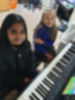 Girls smiling while learning to play piano