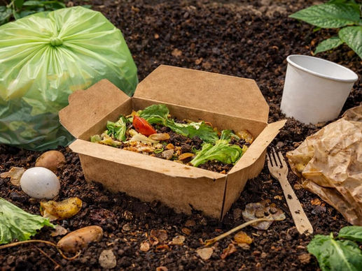 Compostable takeaway packaging partially decomposing in soil, showing food waste and compostable materials during the breakdown process.
