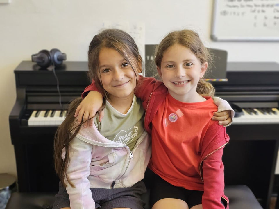 Two young students smiling in front of a piano