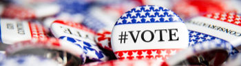 Close-up of patriotic #VOTE buttons with red, white and blue stars, piled together in a campaign-style display.