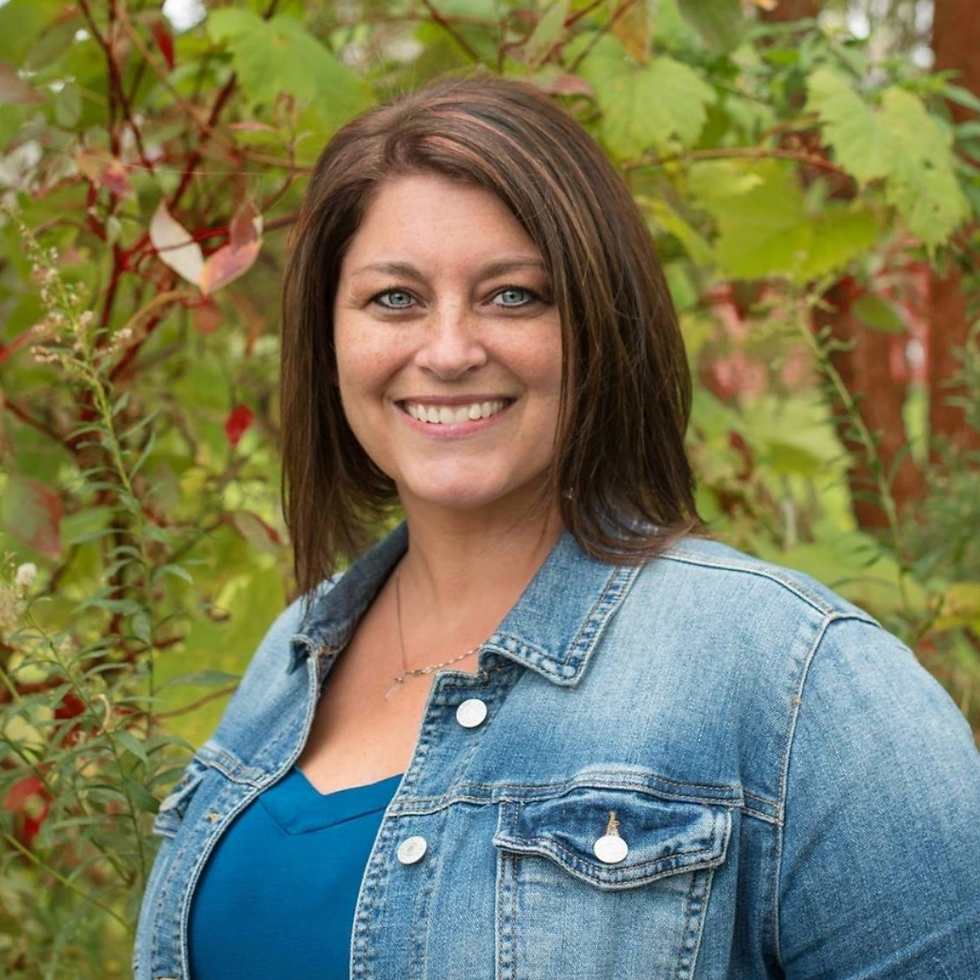 Smiling woman with brown hair in a denim jacket outdoors.