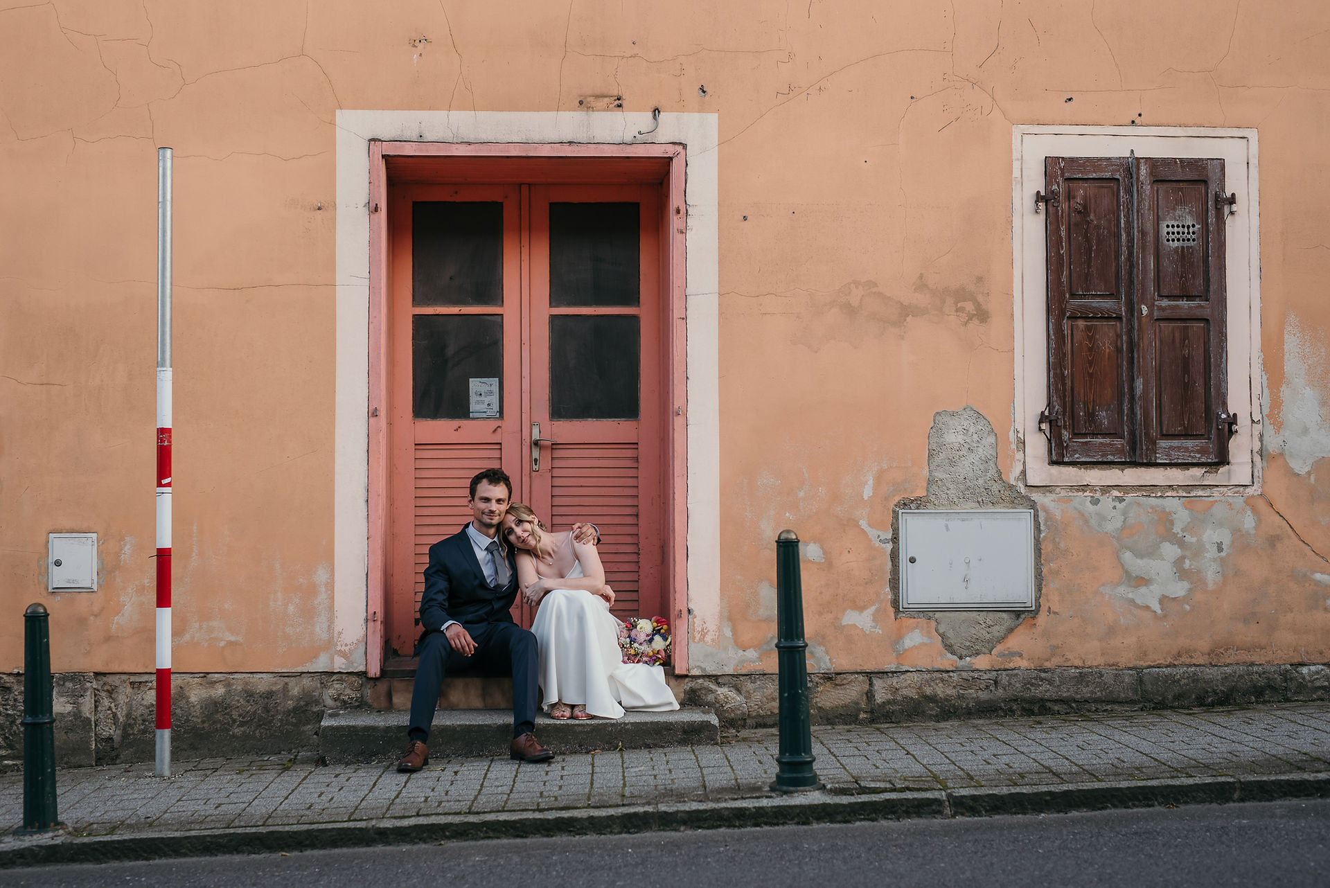 Mladenci sjede na stepenicama ispred pastelnih vrata tijekom fotografiranja u Varaždinskim Toplicama
