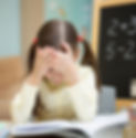 Child feeling frustrated while studying, holding her head in a classroom setting.