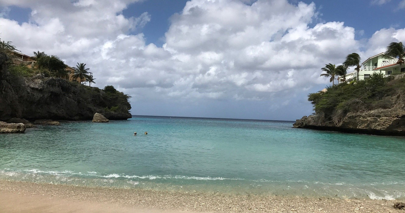 Playa Lagun beach in Curaçao, a small cove with turquoise water, fishing boats, and snorkelers swimming with sea turtles.