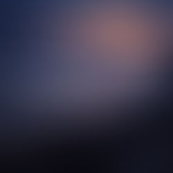 Moody coastal landscape at dusk, viewed from a cliff, with rolling waves, rising white sea mist, and a soft golden-pink glow touching the horizon and water.