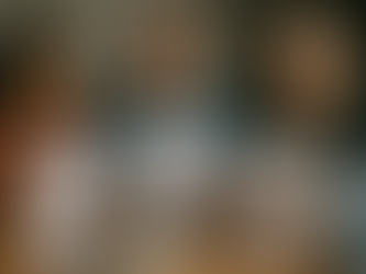 A realistic office photo on November 16: three newcomers sit around a wooden desk with an immigration consultant. One reads a document titled ‘Study Permit Refusal,’ another holds ‘Work Permit Extension Approved,’ and the third reviews a ‘PNP Invitation.’ A small desk calendar shows ‘November 16’ and a laptop with a generic government portal is open. Their candid expressions—concern, relief, and focused attention—reflect mid-November policy changes and mixed outcomes.”