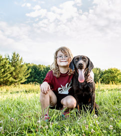 A young girl and her chocolate lab sitting in a field.