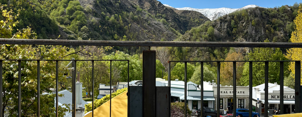View of Arrowtown from a bar. View of mountains and greenery. Table with drinks and plates.