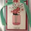 Thumbnail: I love you message under a pink bouquet.  Underneath several layers of pink, mint green, and red, on a white card.  A white stitched mint green ribbon bow sits at the top of the card under another small bouquet.  