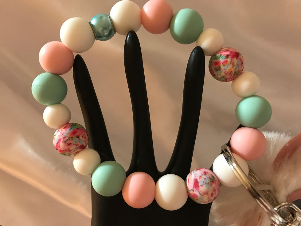 Teal, white, and pink silicone beads in assorted sizes, with three printed pink beads in a floral print with small pink pigs.  A center shinny teal bead with a large key ring and a fluffy white pom pom pig.   He is too cute.