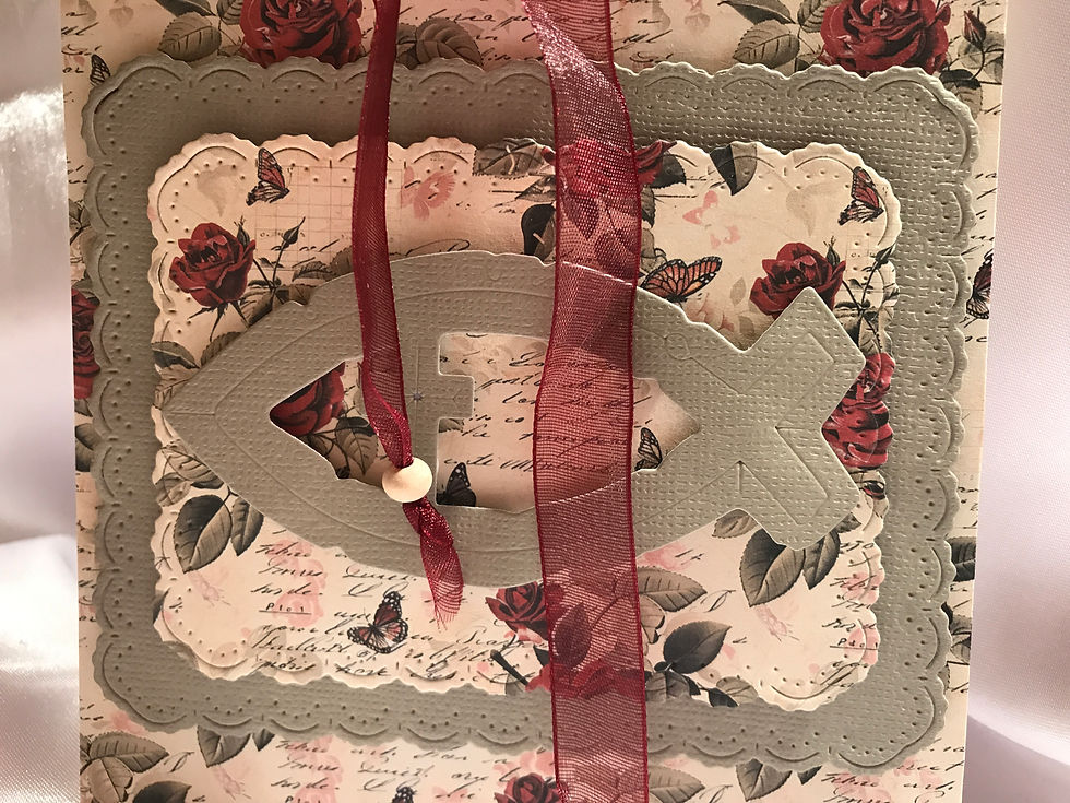 Floral rose paper with grey/green leaves and coordinating christian fish symbol.  Grommets leave a place for a red organza ribbon tied in a bow with wooden beaded ends.