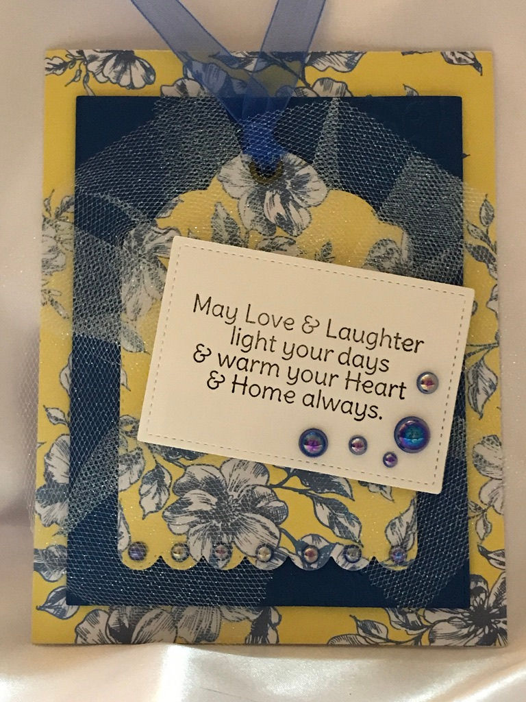 Yellow with blue floral background, a navy stitched die cut rectangle with a large yellow and blue floral matching tag.  The tag has a metal grommet with a blue organza ribbon tie.  In the scalloped bottom of the tag are blue AB blue colored gems.  The white tulle adds a little sparkle sitting on the tag and then a warm sentiment in the center with blue AB gem embellishments finishes the look.  This card is just beautiful.