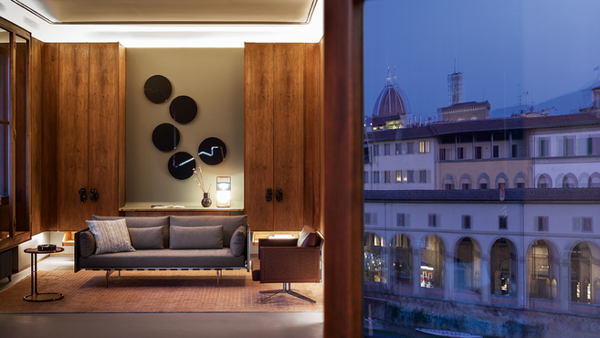 Clayton armchair by Poltrona Frau positioned beside a sofa in a refined living interior with shelving, small tables and wall mirrors highlighting the designer lounge armchair