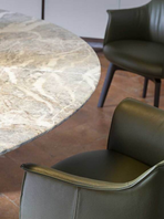 Archibald dining chair positioned beside a round dining table, showing its curved backrest and enveloping seat within a refined dining environment