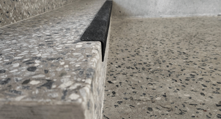 Macro of terrazzo step edge with black slip-resistant insert meeting polished concrete landing.