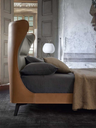 Side view of the Mamy Blue bed highlighting the high upholstered headboard and enveloping silhouette within a curated bedroom