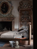 Volare Due bed positioned in a classic interior with fireplace, emphasizing its elevated structure and tailored upholstery