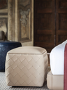 Grant ottoman 65x45 by Poltrona Frau placed beside a bed in a bedroom setting highlighting its quilted leather surface and compact form