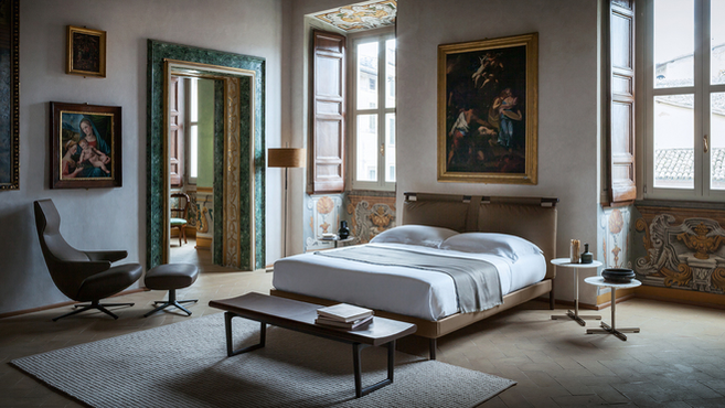 Times bed by Poltrona Frau styled in an elegant bedroom interior with lounge chair and bench, highlighting the upholstered bed within a refined residential environment